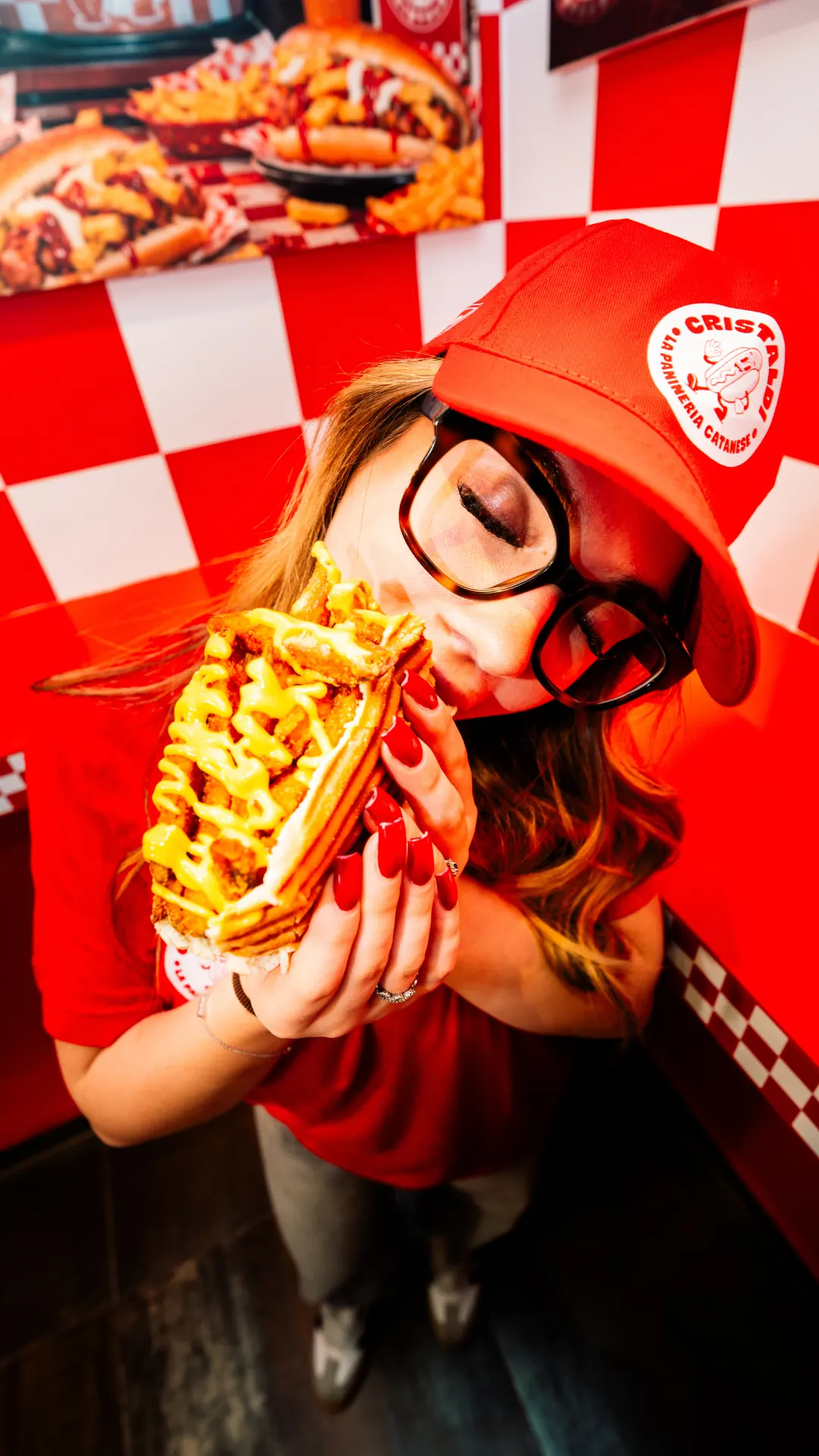 ragazza col cappellino cristaldi che addenta un panino nel locale a scacchi